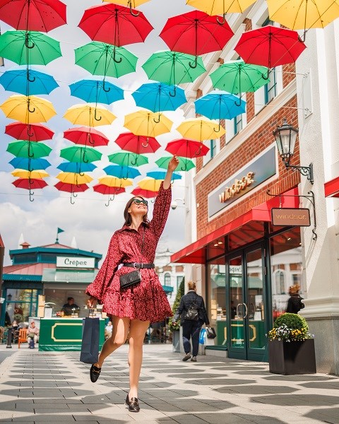 Eine Frau unter bunten Regenschirmen im Designer Outlet Neumünster