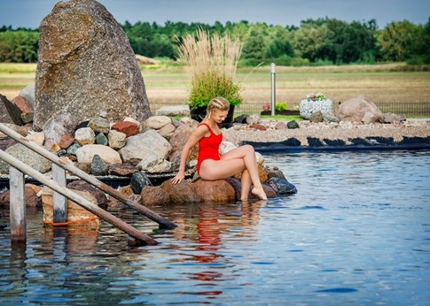 Eine Frau sitzt auf Steinen mit den Füssen im Wasser des Außenbeckens der Kristall Therme Bad Wilsnack