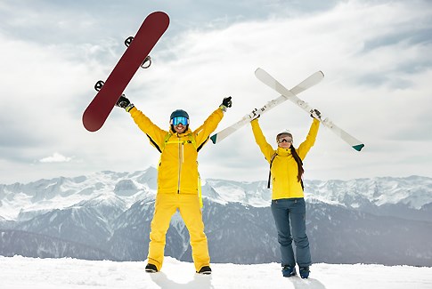 Zwei Skifahrer in Gelb heben ihre Skier und Snowboards in die Luft