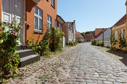 Bunte Fassaden und Stockrosen in den Gassen der Altstadt von Ebeltoft, Djursland, Dänemark in der Sonne vor blauem Himmel