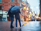 Zwei Personen unter einem Regenschirm in einer nassen Straße in Amsterdam bei Abendlicht.