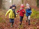 Drei Kinder, die gemeinsam durch einen herbstlichen Wald laufen