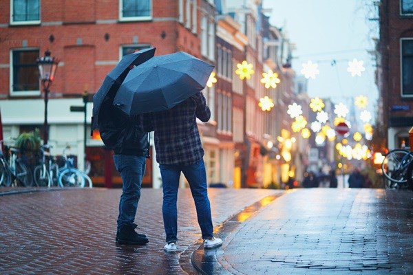 Zwei Personen unter einem Regenschirm in einer nassen Straße in Amsterdam bei Abendlicht.