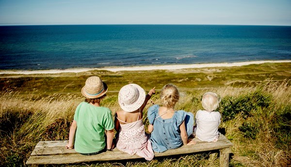 Vier kleine Kinder sitzen im Sommer auf einer Bank und blicken aufs Meer