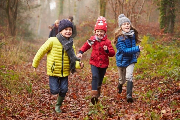 Drei Kinder, die gemeinsam durch einen herbstlichen Wald laufen