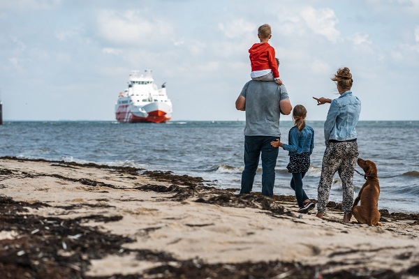Eine Familie mit Kindern und Hund betrachtet die FRS Syltfähre vom Strand aus