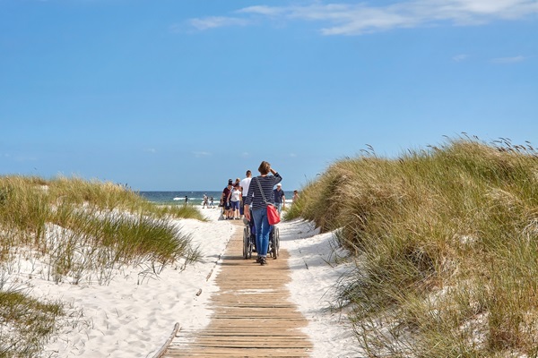 Eine Frau schiebt einen Rollstuhl zum Strand von Dueodde auf Bornholm