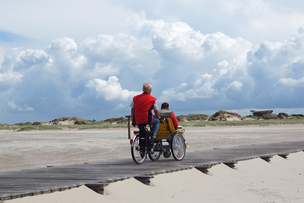 Zwei Männer auf einem Rollstuhl-Fahrrad auf dem Radweg zum Strand