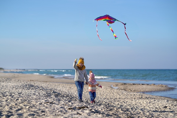 Zwei kleine Kinder mit Schal und Mütze lassen einen Drachen am Strand steigen