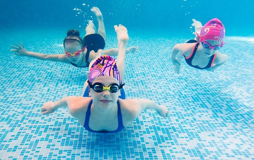 Kinder tauchen mit bunten Badekappen im Schwimmbad