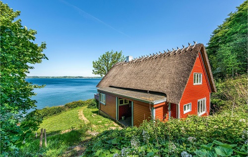 Reetgedektes rotes Ferienhaus vor blauem Meer und Himmel
