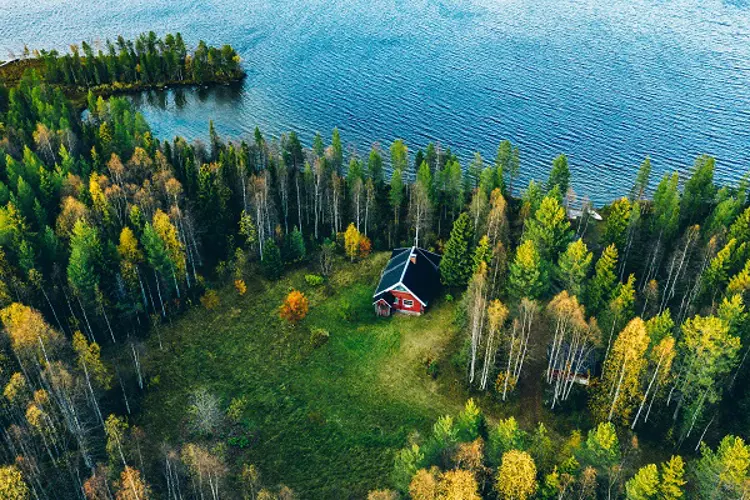 Luftaufnahme eines roten Blockhauses mit Sauna im Frühlingswald am See in Finnland