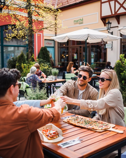 Zwei Paare stoßen an und essen Pizza im Designer Outlet Neumünster