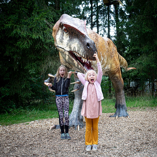 Zwei Mädchen hüpfen begeistert vor einem Dino im Dinosaurierpark im GIVSKUD ZOO – ZOOTOPIA