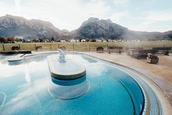 Außenbecken der Königlichen Kristalltherme Schwangau mit Bergen und Häusern im Hintergrund