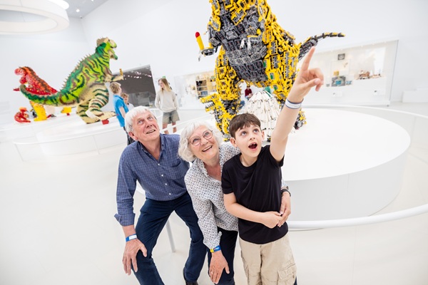 Großeltern betrachten gemeinsam mit ihrem Enkelkind LEGO® Dinosaurier im LEGO® House