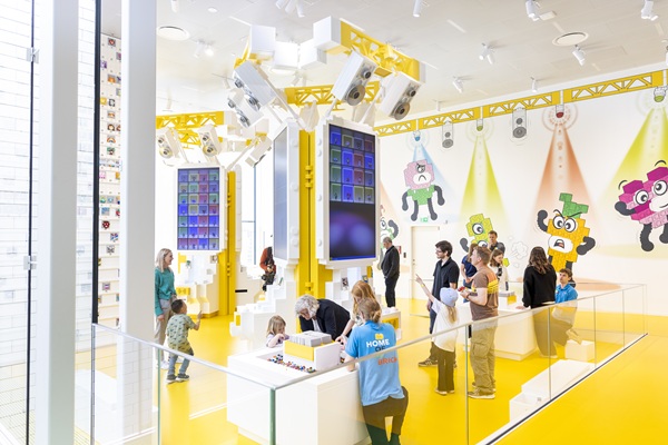 Kinder und Erwachsene erkunden die gelbe Erlebniszone im LEGO® House