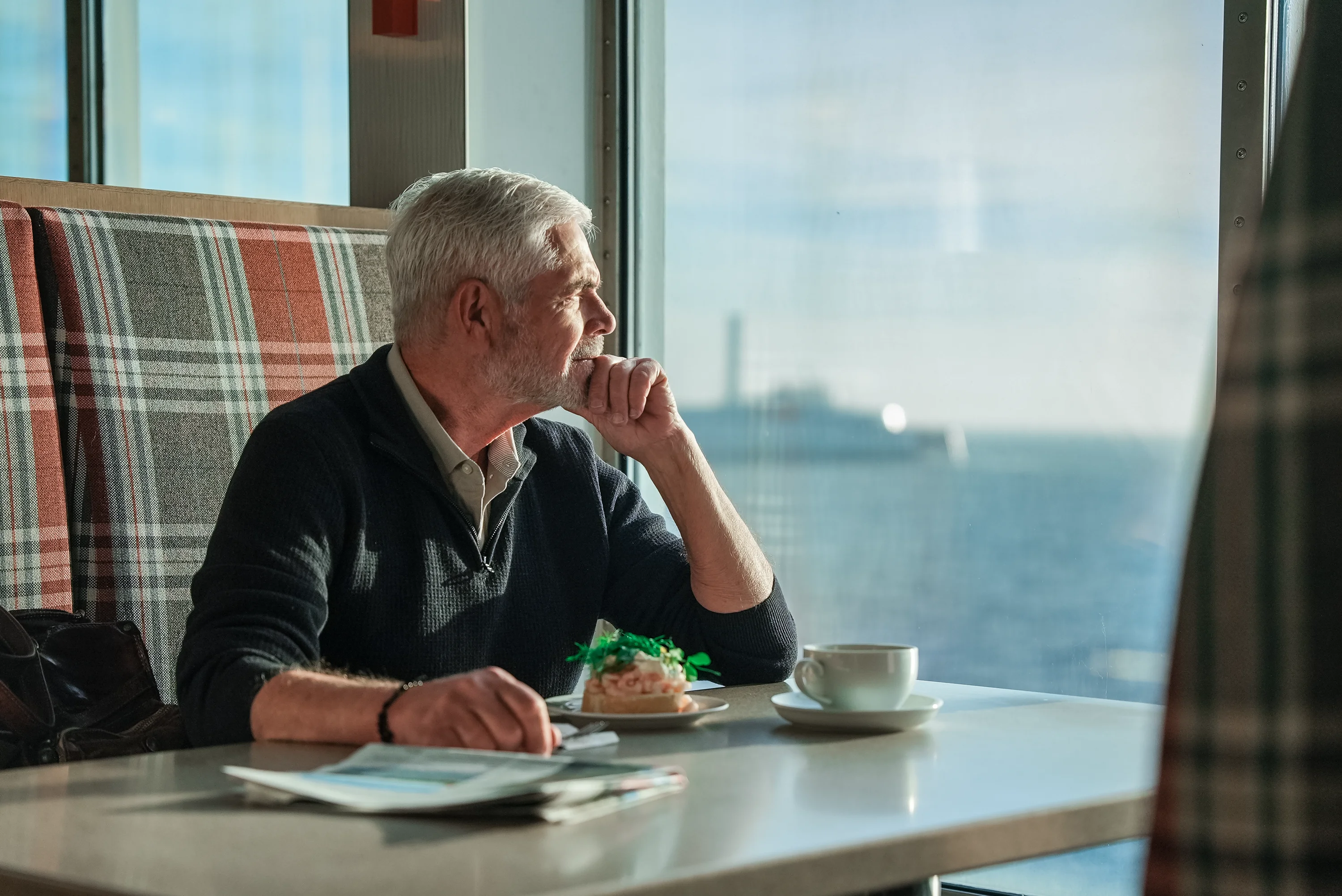 Ein Mann genießt bei Kaffee und einem belegten Brötchen den Meerblick an Bord einer Scandlines-Fähre