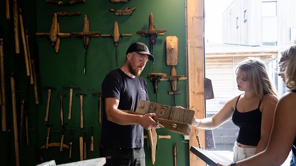 Ein Mann zeigt Frauen ein Holzwerkzeug in der Werkstatt des Wikingerschiffsmuseums in Roskilde
