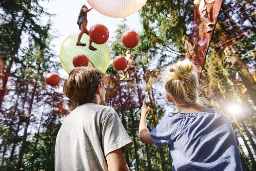 Kinder spielen mit Bällen in einem großen Netz hoch oben in den Bäumen im WOW PARK